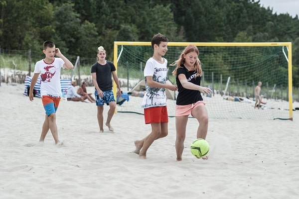 dzieci grają w piłkę na piaszczystym boisku na plaży